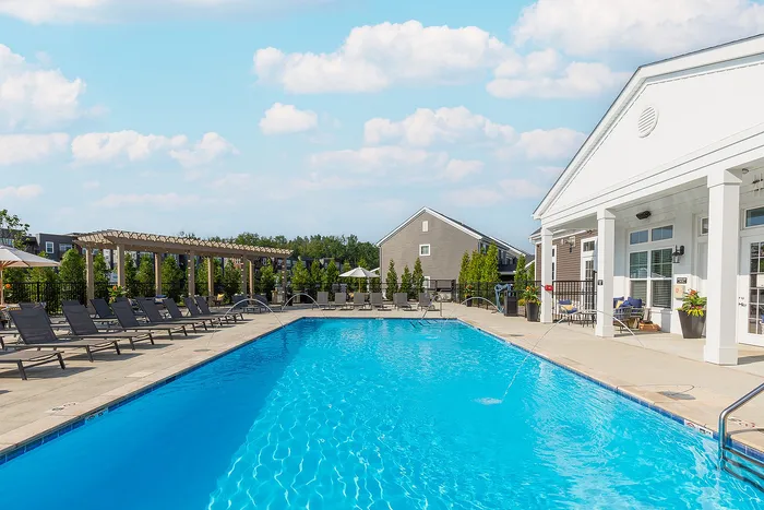 Luxurious apartment complex featuring a sparkling pool with elegant sun loungers, surrounded by lush greenery and modern architecture.