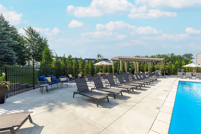 Luxurious outdoor pool area with elegant lounge chairs, vibrant potted plants, and a scenic garden backdrop under a sunny sky.