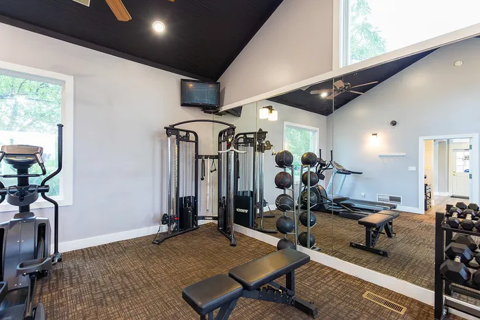 Modern fitness room equipped with state-of-the-art exercise machines, benches, and a wall of mirrors, offering a bright and inviting workout space.