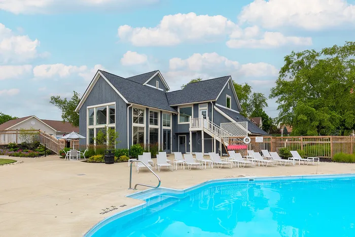 Charming modern clubhouse with large windows by the pool, surrounded by vibrant greenery and ample lounge chairs.