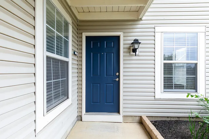 Inviting apartment entrance with a striking blue door, elegant outdoor lighting, and charming window accents.