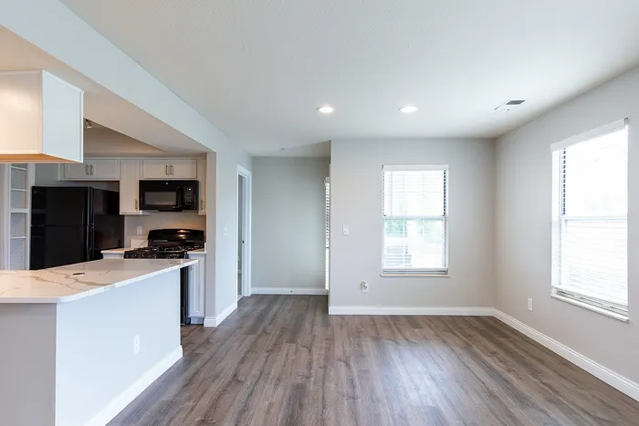 Modern apartment featuring an open-plan kitchen with sleek cabinetry, adjacent to a bright living area with large windows and stylish wood flooring.