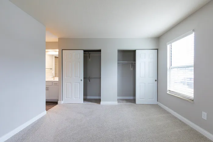 Bright and spacious bedroom with dual closets and natural light streaming through a large window, creating a serene living space.