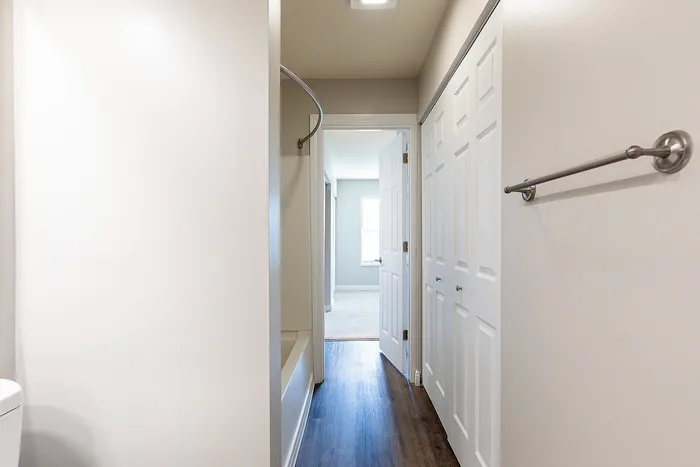 Bright and inviting hallway with elegant wood flooring, leading to a sunlit room, showcasing a modern bathroom with sleek fixtures.