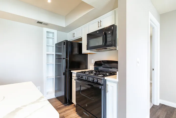 Bright and modern kitchen featuring sleek black appliances, pristine white cabinetry, and elegant wooden flooring.