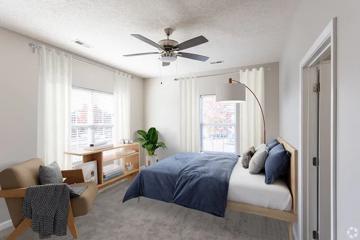 Bright, modern bedroom with a stylish bed, armchair, ceiling fan, and large windows.