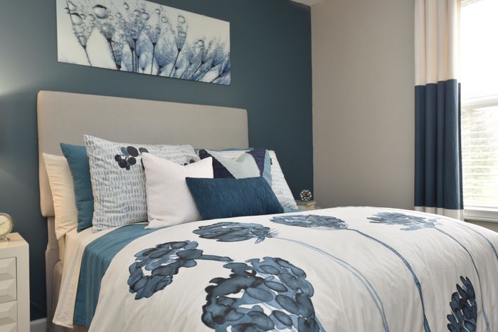 Elegant bedroom with a plush bed adorned with blue and white accent pillows and floral bedding, complemented by modern artwork.