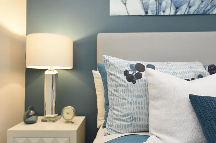 Chic bedroom with modern decor, featuring a stylish gray headboard, patterned pillows, and a bedside lamp.