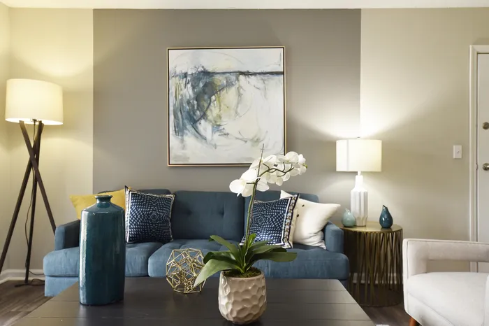 Elegant living room with a modern blue sofa, abstract wall art, decorative cushions, and chic lighting.