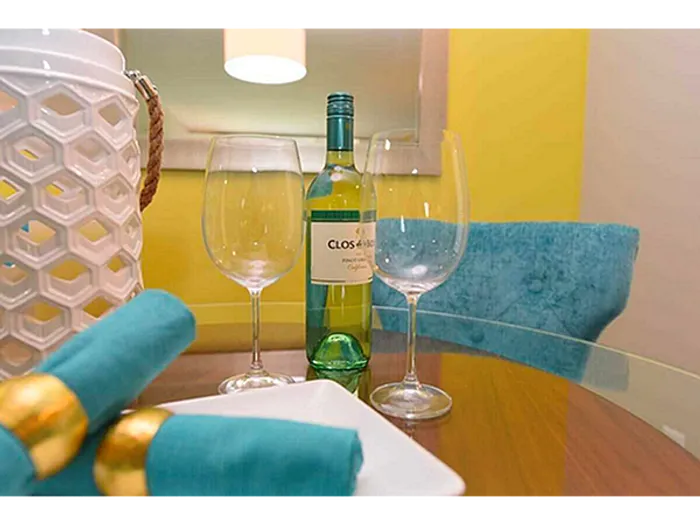 Elegant dining setup featuring a bottle of wine, two wine glasses, and blue napkins on a glass table.