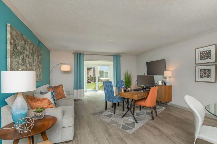 Contemporary living room with stylish decor, featuring a cozy sofa, vibrant cushions, a desk area, and large window views.