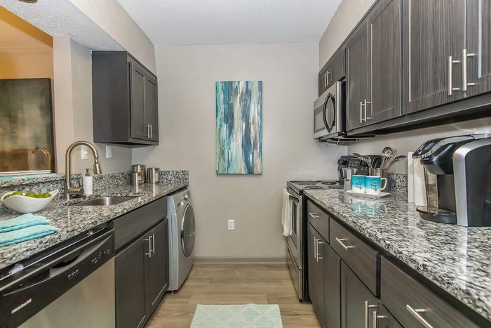 Modern kitchen with dark cabinetry, granite countertops, stainless steel appliances, and a stylish abstract painting.