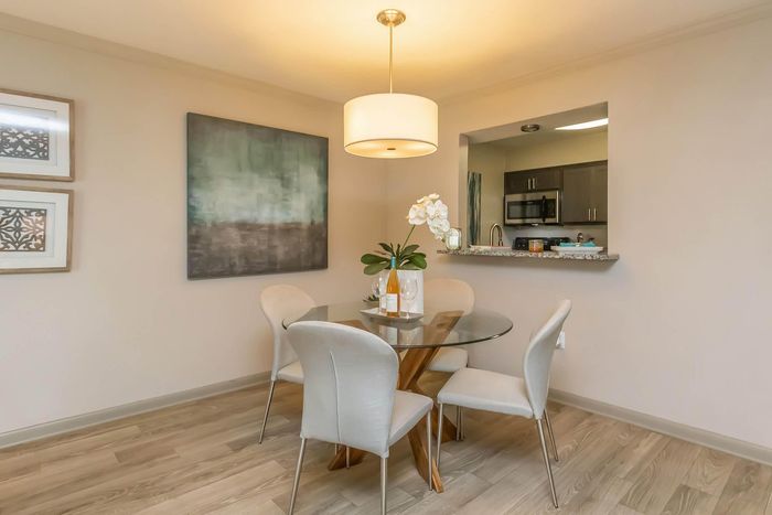 Elegant dining space with a glass table and modern chairs, featuring stylish decor and an open view to the kitchen.