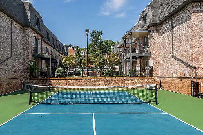 Inviting residential tennis court nestled between elegant brick buildings, surrounded by lush greenery.