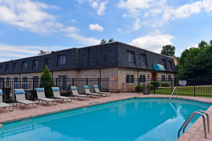 Beautiful apartment building with a pristine swimming pool and lounge chairs, surrounded by greenery.
