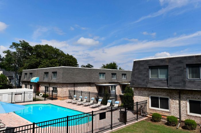 Sunny apartment complex featuring a pristine outdoor pool and lounge area with comfortable sun chairs.