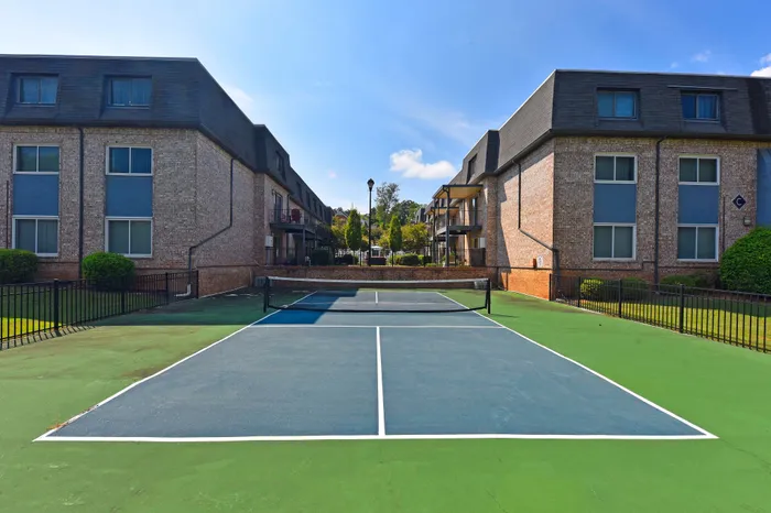 Beautiful tennis court surrounded by modern brick apartment buildings under a clear blue sky.