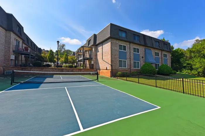 Charming apartment building with a well-maintained tennis court under a clear blue sky.