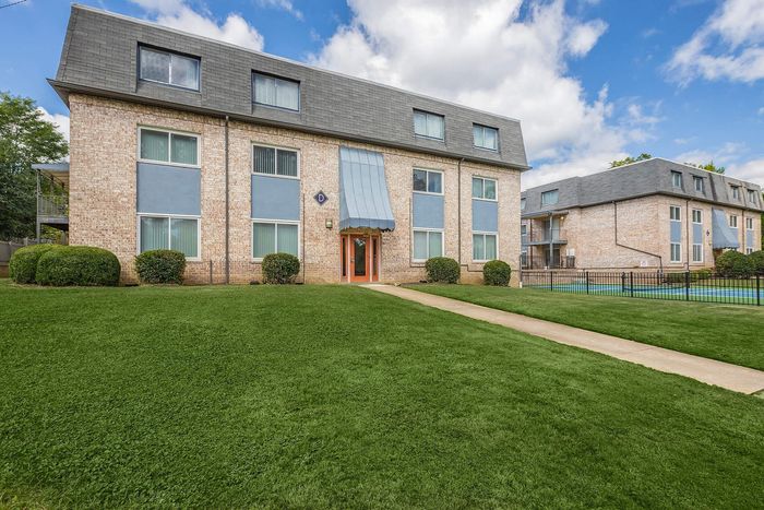 Inviting brick apartment building with lush green lawns and large windows.
