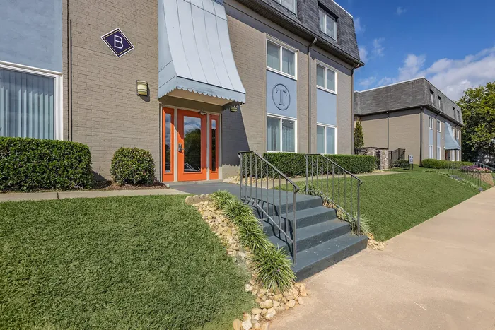 Attractive apartment building with inviting orange door, neatly trimmed hedges, and clear blue sky.
