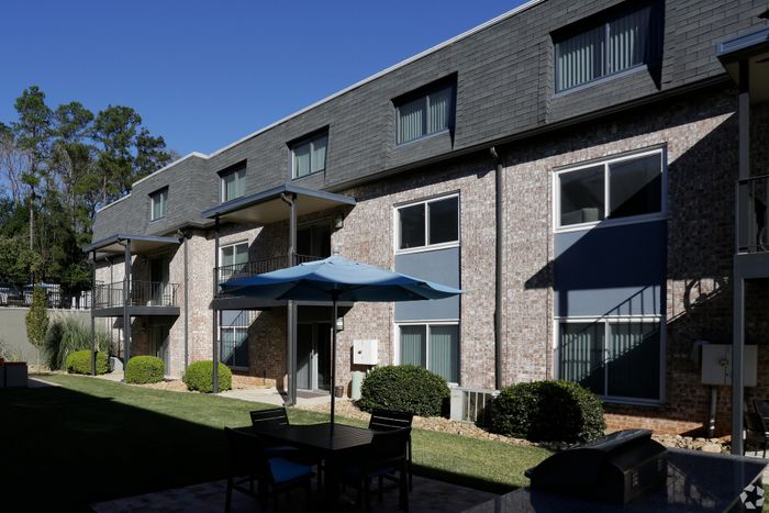 Elegant brick apartment building with large windows and a cozy patio area featuring outdoor seating and a parasol.