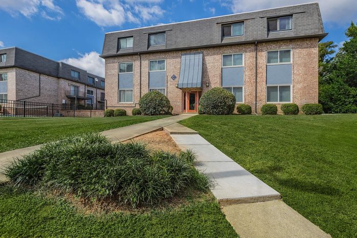 Elegant brick apartment building with lush green lawn and clear blue sky.