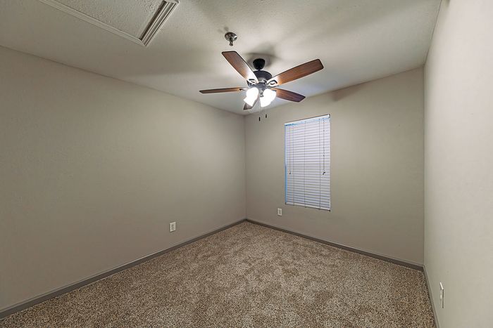 Inviting bedroom with plush carpet flooring, ceiling fan, and natural light from window blinds.