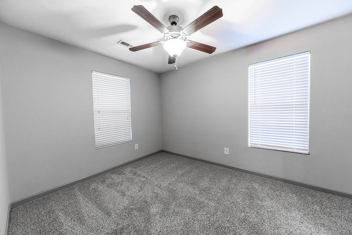 Inviting bedroom with carpeted floor, ceiling fan, and natural lighting from two windows.
