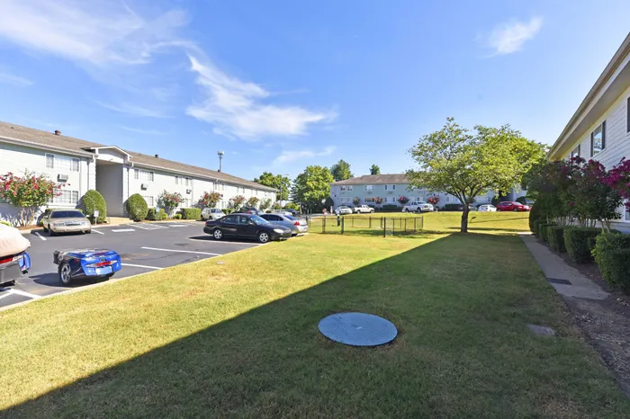 Bright exterior view of a well-maintained apartment complex with ample parking and lush greenery.