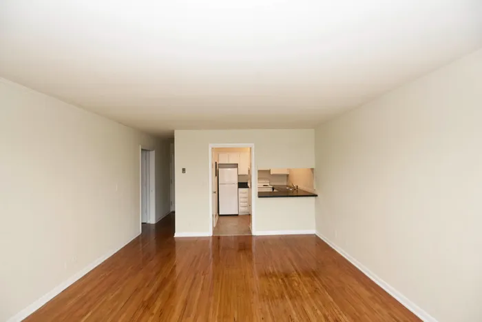 Bright and spacious living area with polished hardwood floors and a compact kitchen view.