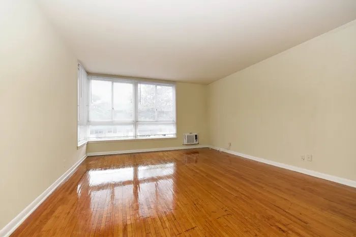 Open, empty room with large windows and polished hardwood floors.