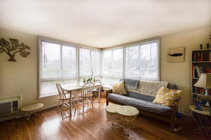 Inviting living area with a sunlit corner featuring large windows, comfortable seating, and a charming dining nook.