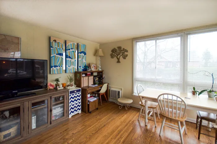 Cozy living room with wooden floors, a modern TV setup, artistic decor, and a bright dining area.