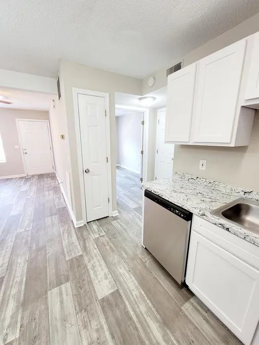 Bright kitchen view with granite countertops, sleek cabinetry, and a stylish laminate floor extending to the hallway.