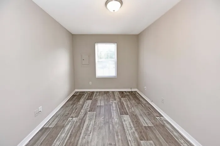 Bright, empty room with stylish wood flooring and neutral walls, featuring a single window letting in natural light.
