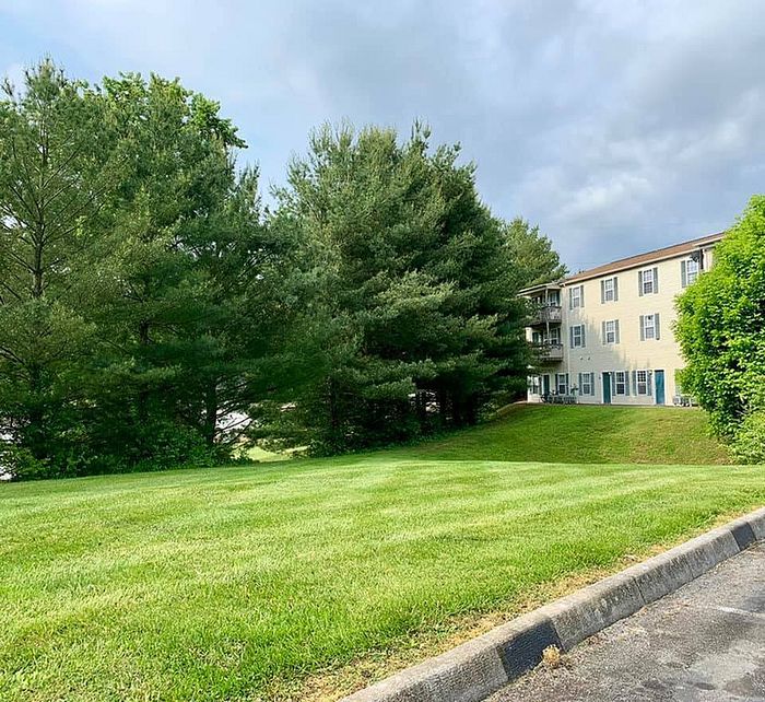 Charming apartment building surrounded by lush greenery and manicured lawns under a cloudy sky.