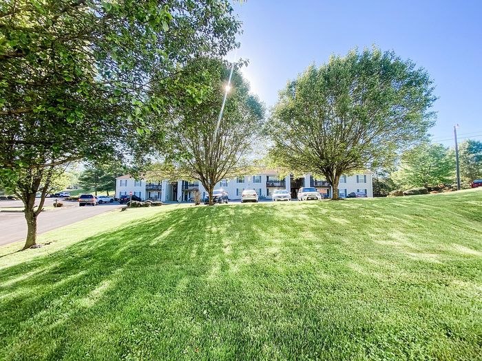 Charming apartment complex surrounded by lush greenery and spacious lawns under a clear blue sky.