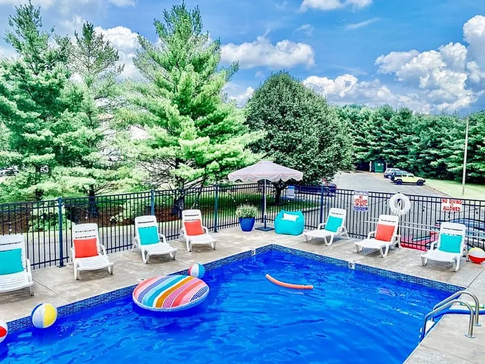 Vibrant outdoor pool area with colorful lounge chairs and inflatable pool toys surrounded by lush greenery.