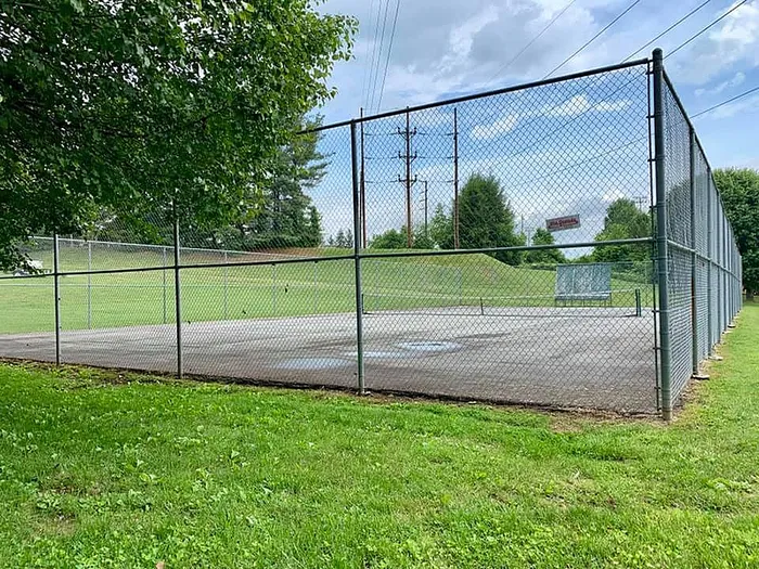 Inviting outdoor tennis court enclosed by greenery and sturdy fencing under a clear blue sky.