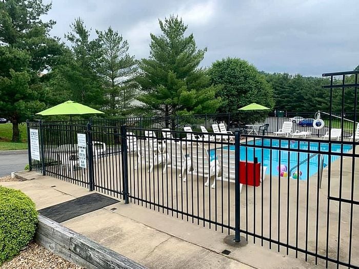 Charming outdoor pool area with sun loungers and green umbrellas surrounded by lush trees.