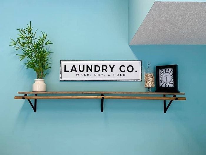 Stylish laundry room shelf with a plant, vintage clock, and laundry-themed sign on a turquoise wall.