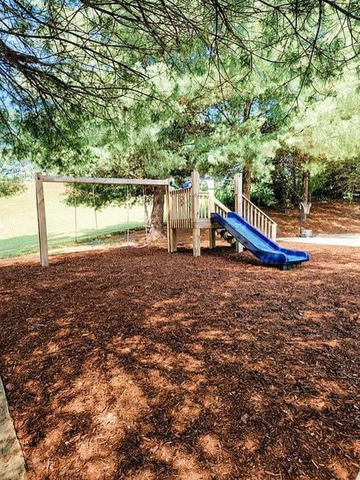 Inviting playground with a wooden structure, slide, and swings surrounded by lush trees.