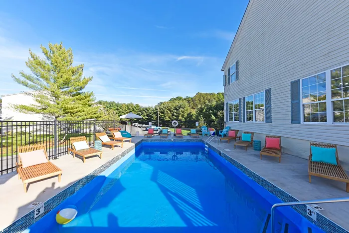Inviting swimming pool area with colorful sun loungers, surrounded by lush greenery and clear blue skies.