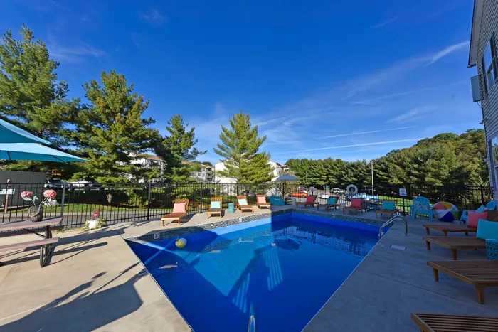 Inviting outdoor pool scene with sun loungers and vibrant umbrellas surrounded by lush greenery.