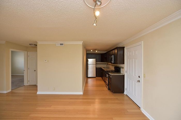 Modern apartment interior showcasing an open kitchen with sleek cabinets and a bright living space with hardwood floors.