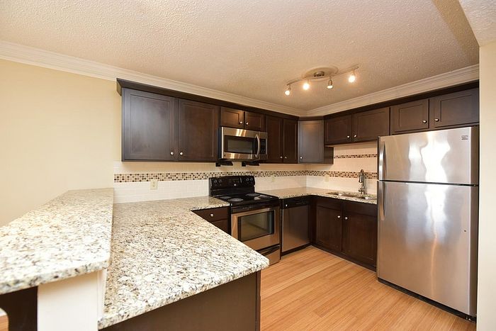 Elegant kitchen with modern appliances, dark wood cabinets, granite countertops, and track lighting.