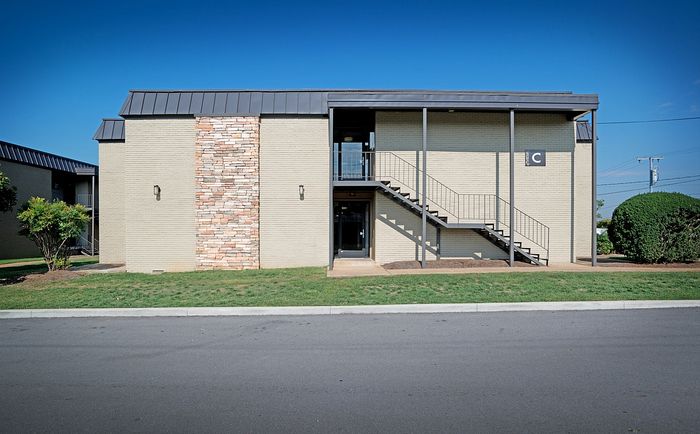 Modern apartment building exterior with brick accents and metal stairway under clear blue sky.