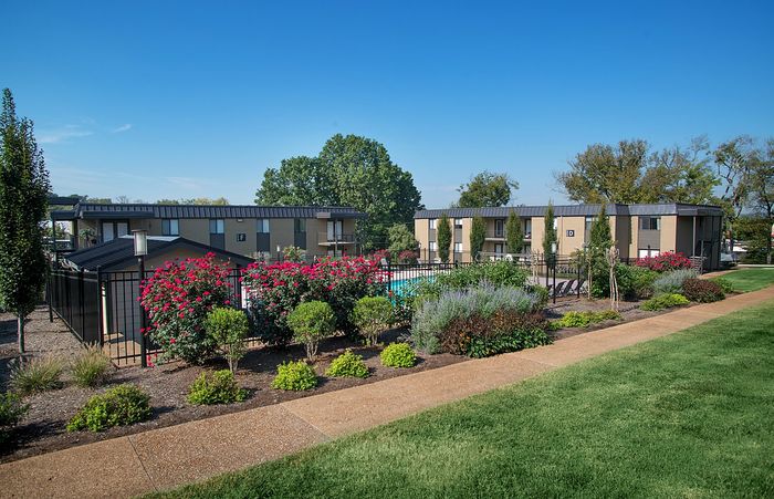 Beautiful apartment complex with lush gardens and manicured pathways under a clear blue sky.