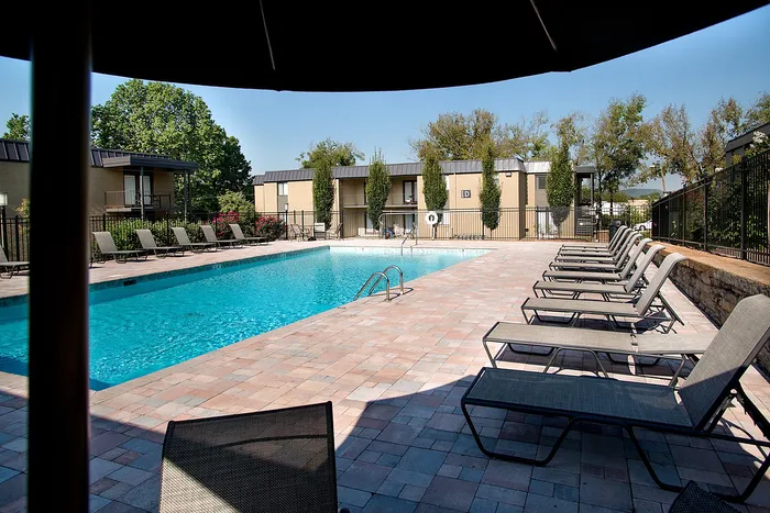 Inviting pool area with modern sun loungers and lush greenery in a tranquil apartment complex setting.