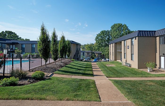 Beautiful apartment complex with lush landscaping, a pool, and sunny walkways.